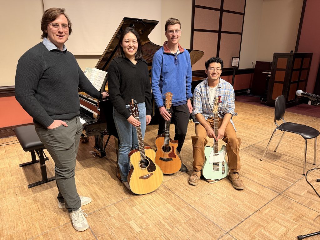 Four students in front of a piano on stage.